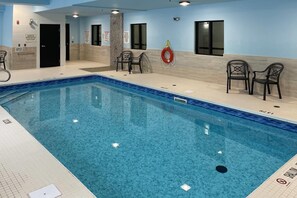 Una piscina interior con agua cristalina, sillas negras y señales de seguridad en las paredes.
