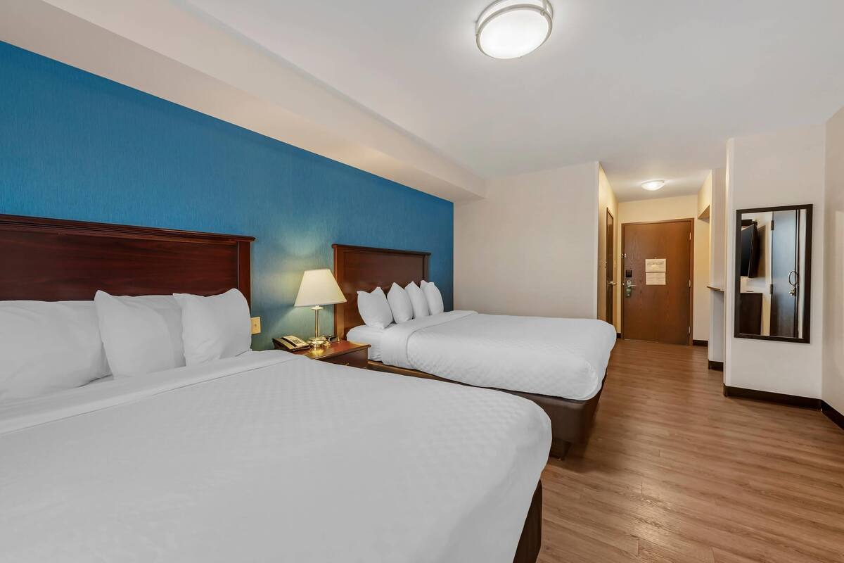Habitación de hotel con dos camas, suelo de madera, pared azul decorativa, televisor y puerta que da a otra habitación.