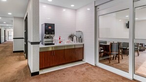 A modern kitchen with a coffee machine, a water dispenser, and a small plant on the counter.