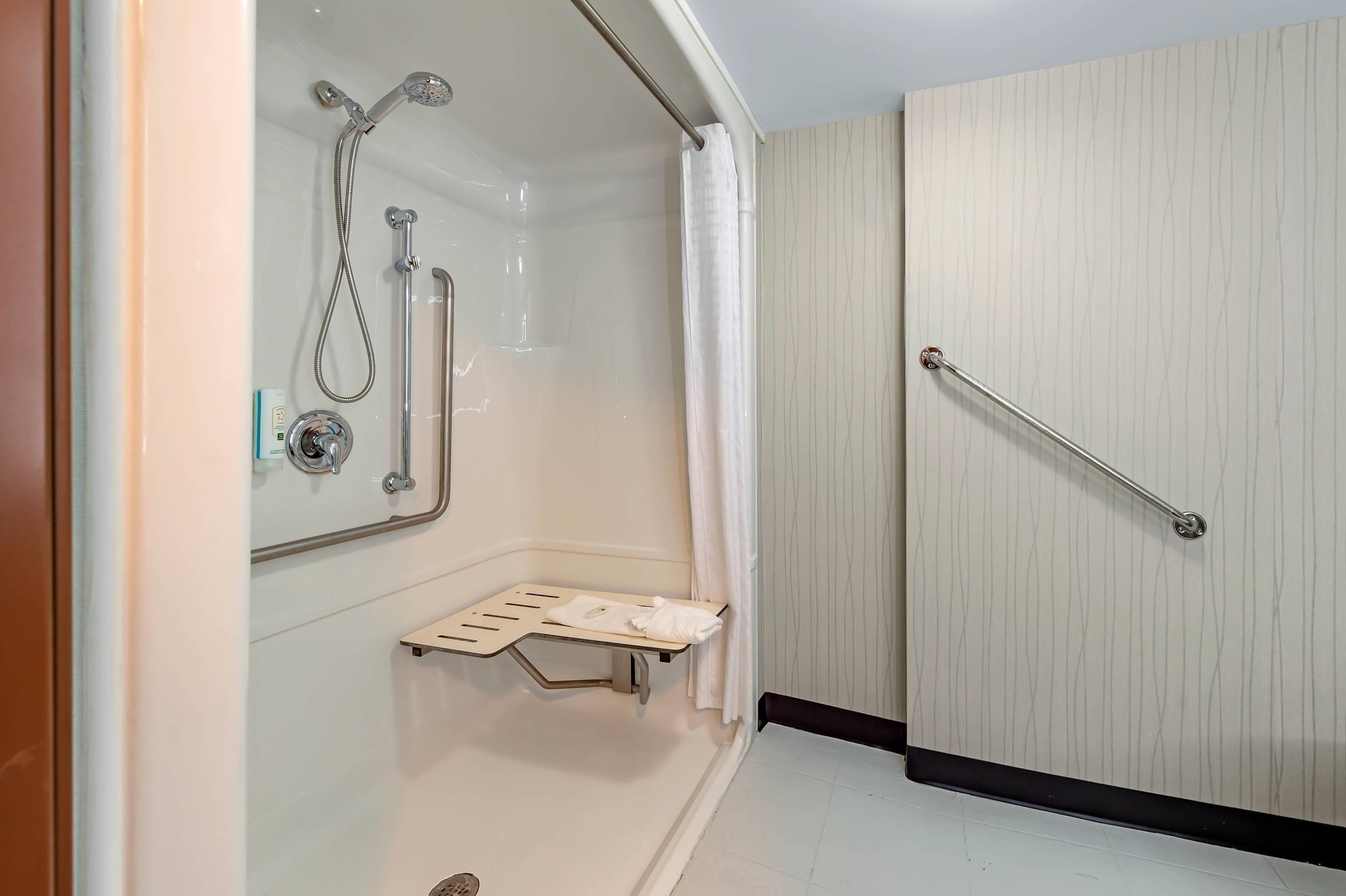 A shower with a handheld showerhead, a handheld shower, and a grab bar.
