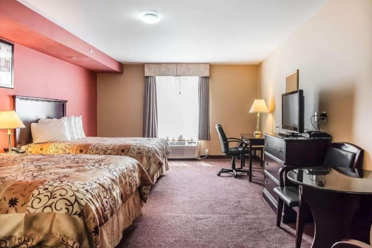 Habitación de hotel con dos camas, un escritorio con silla, un televisor y un ventanal con cortinas.
