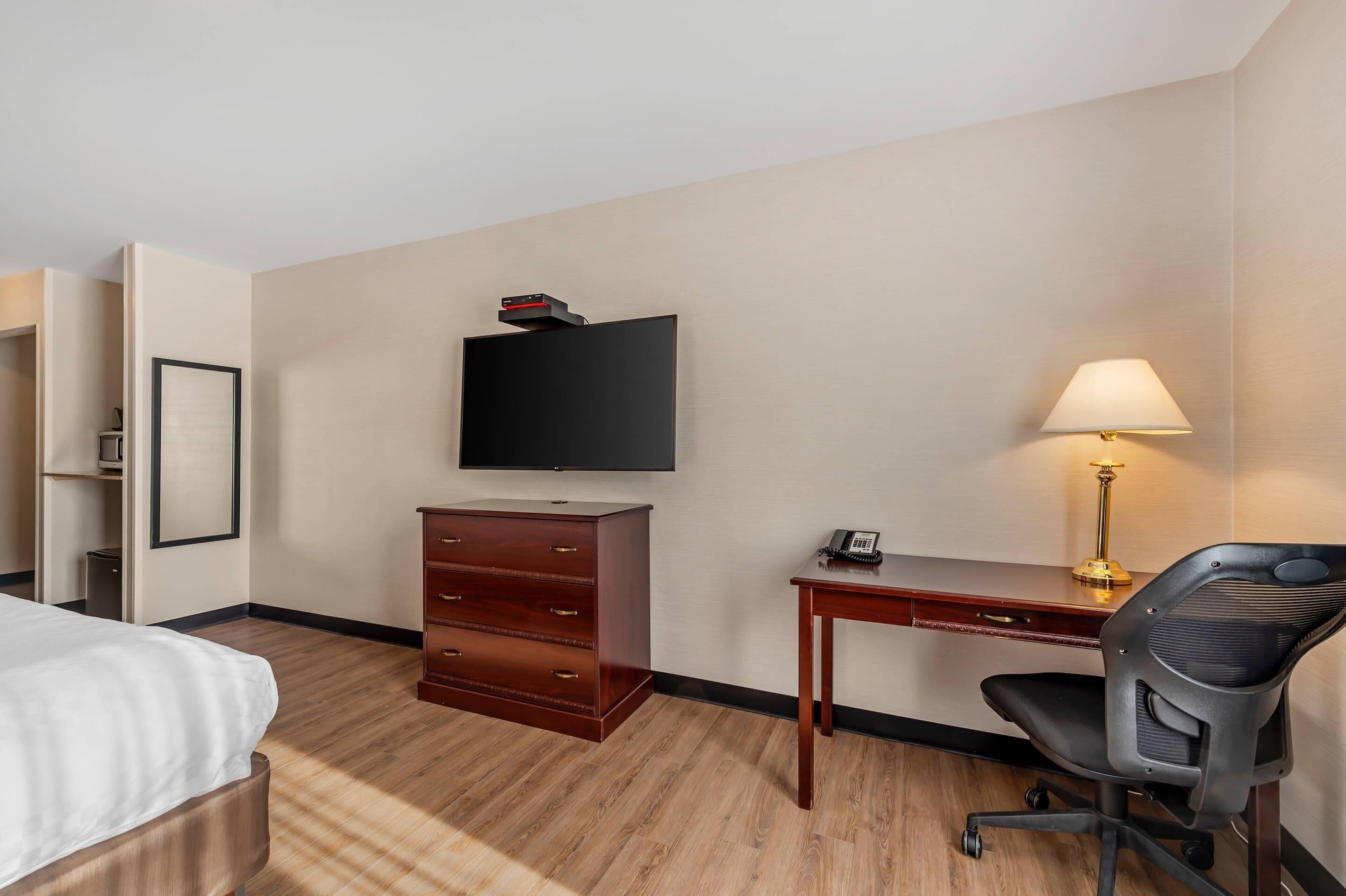 A hotel room with a bed, a desk with a lamp, a chair, a television, and a dresser.