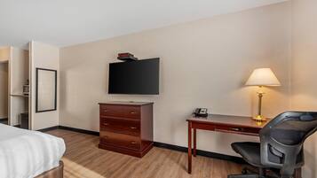 A hotel room with a bed, a desk with a lamp, a chair, a television, and a dresser.