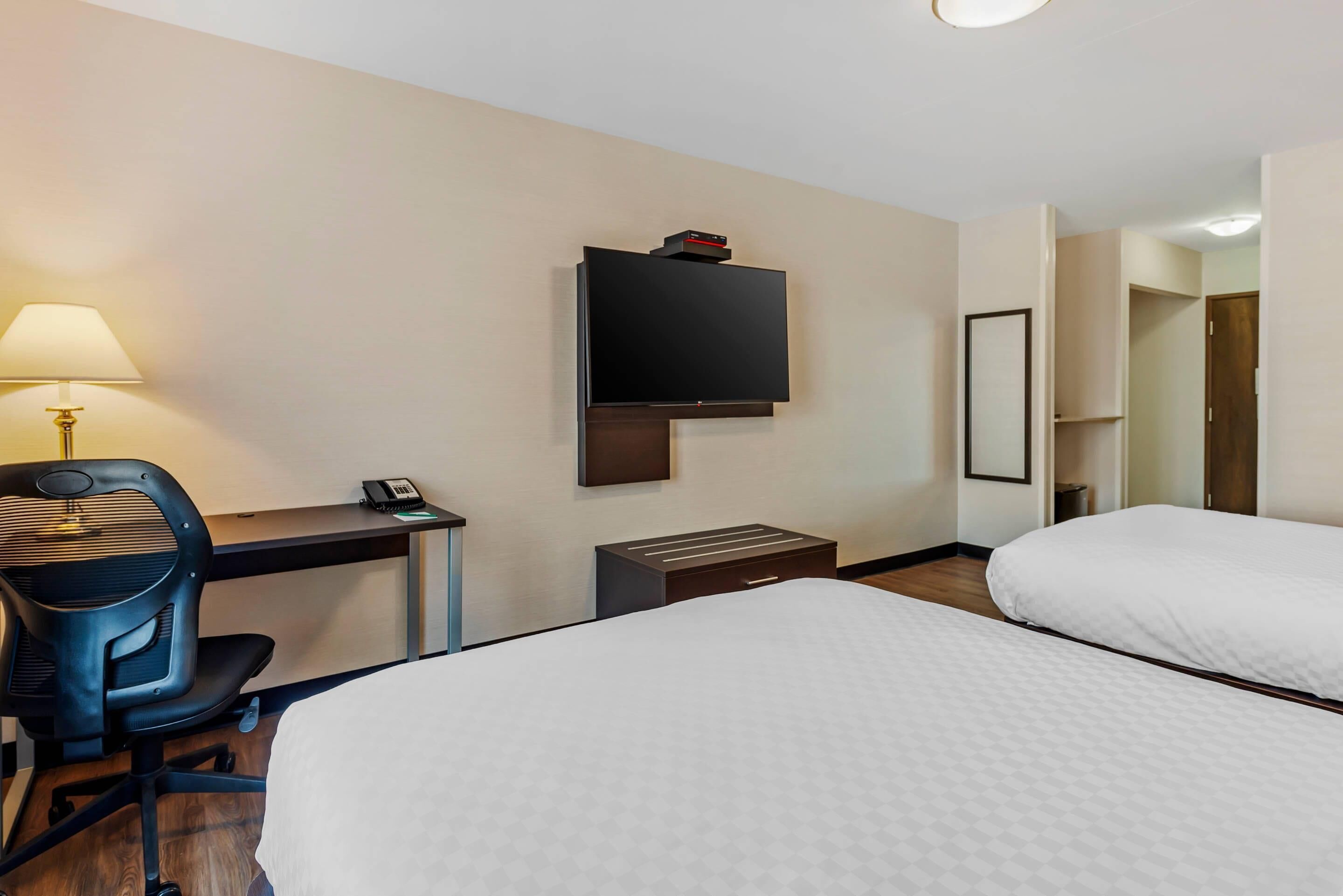 Une chambre d’hôtel comprenant un lit, un bureau avec une lampe, un téléviseur fixé au mur et un petit meuble de rangement.