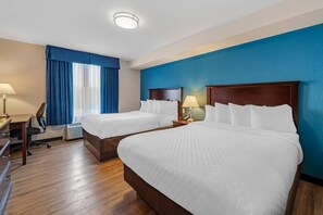 Habitación de hotel con dos camas, un escritorio, una silla y una ventana con cortinas.