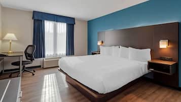 A hotel room with a large bed, a desk, a chair, a lamp, and a window with curtains.