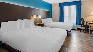 Ein Hotelzimmer mit zwei Betten, einem Schreibtisch, einem Stuhl, einem Nachttisch und einem Fenster mit blauen Vorhängen.