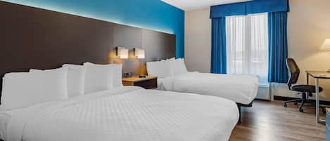 A hotel room with two beds, a desk, a chair, a nightstand, and a window with blue curtains.
