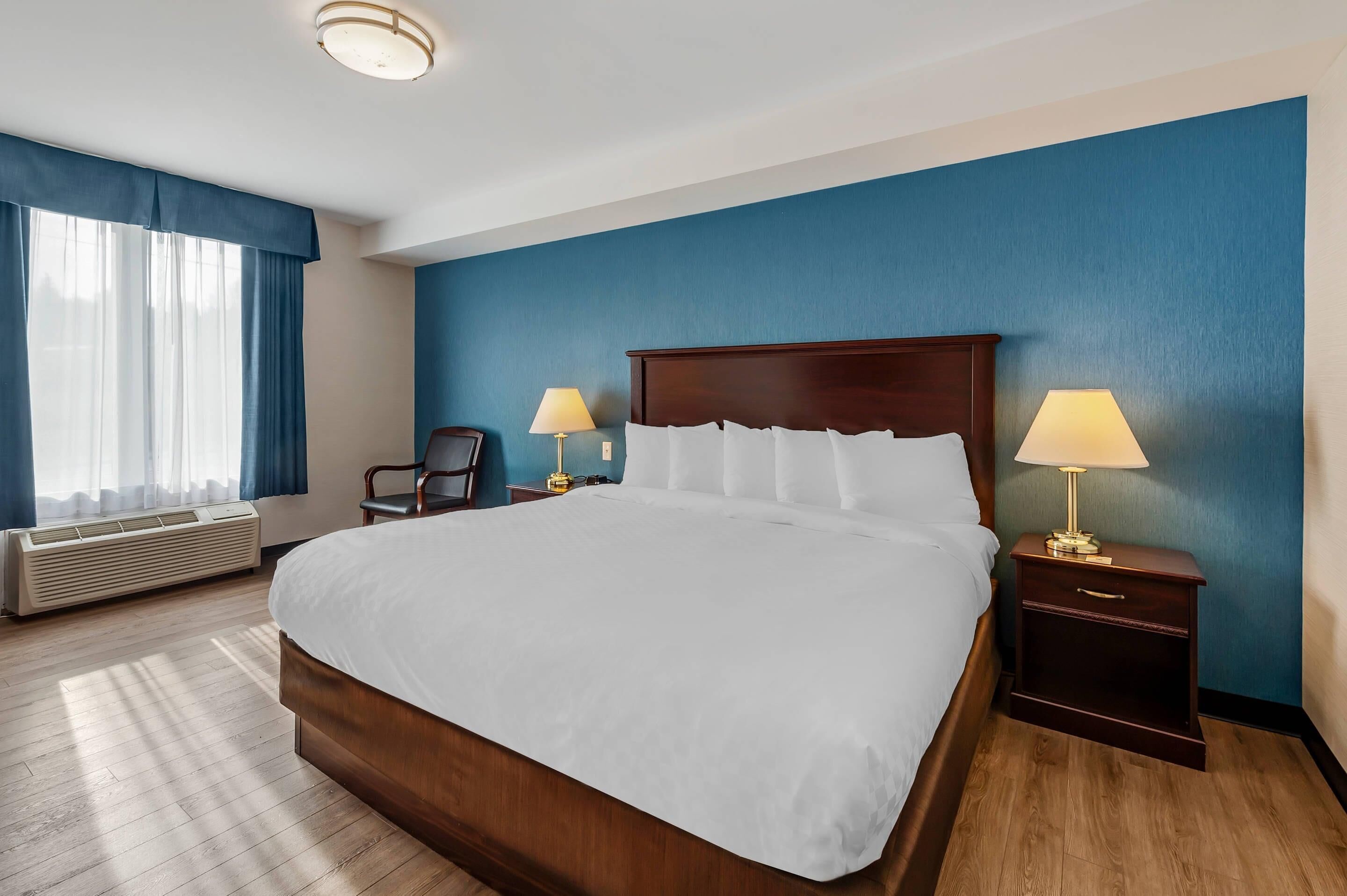 Una camera d'albergo con un letto grande, due comodini con lampade, una sedia e una finestra con tende.