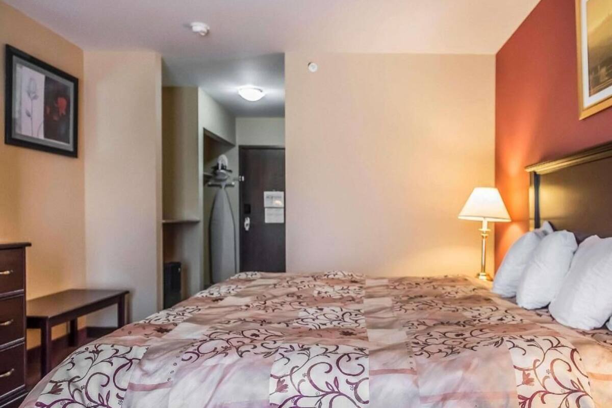 Habitación de hotel con cama, lámpara de noche, cómoda y puerta que da a un pasillo.