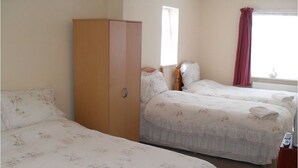 Une chambre avec deux lits simples, dotée de draps à motifs floraux, d’une armoire en bois, d’une fenêtre avec un rideau rouge et d’un radiateur.