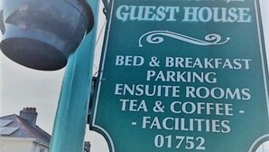 Une pancarte verte indique l’emplacement de l’Alma Lodge Guest House et propose des chambres avec petit-déjeuner et salle de bains privative, un parking, ainsi que du thé et du café, et mentionne les équipements disponibles.