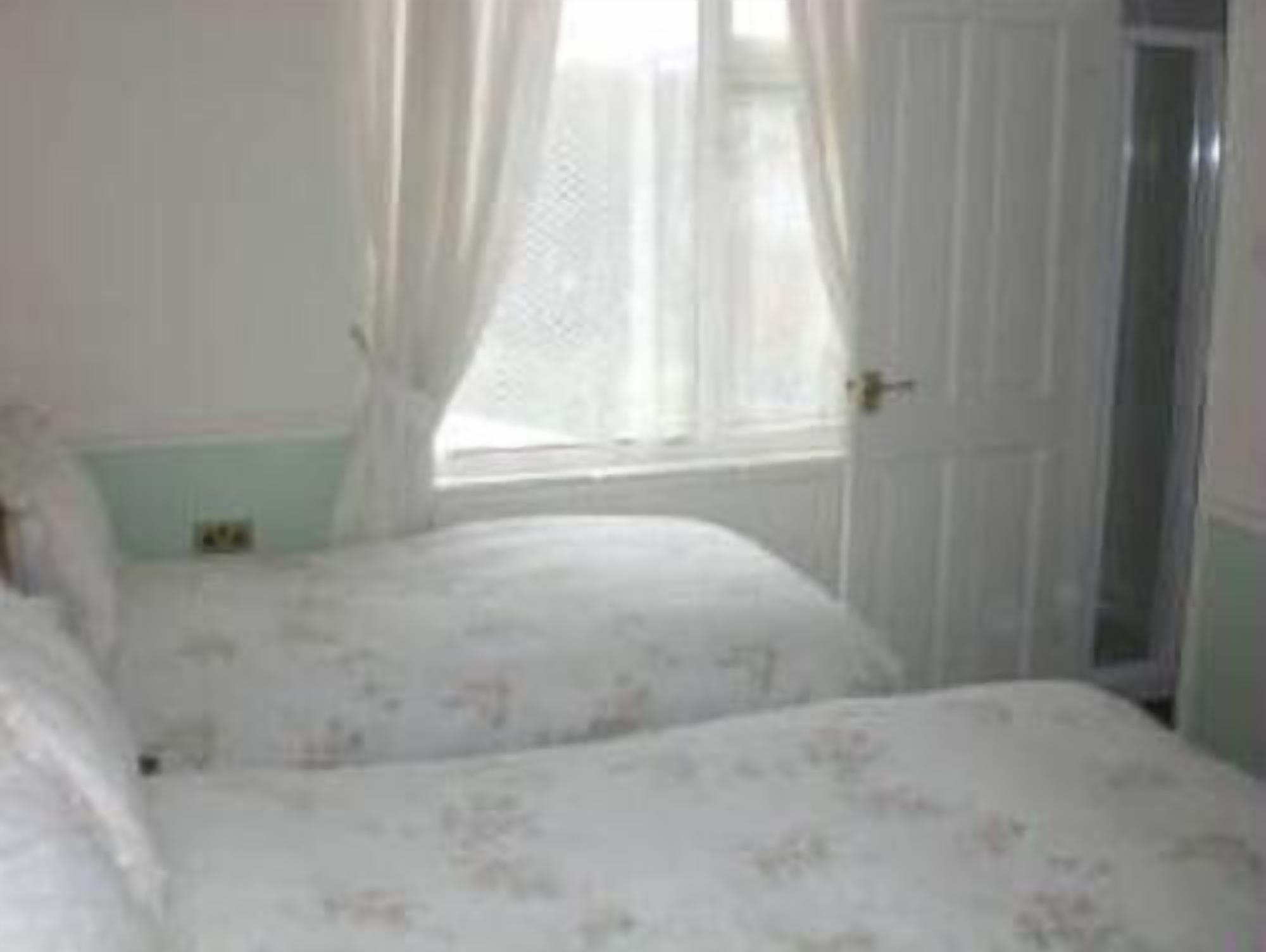 A bedroom with two beds, a window with sheer curtains, and a door.