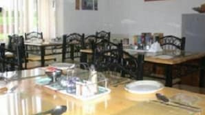 Un espace repas avec des tables et des chaises en bois, un réfrigérateur et divers objets disposés sur les tables.