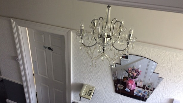 Une pièce avec une porte blanche, un lustre, un miroir et un radiateur.