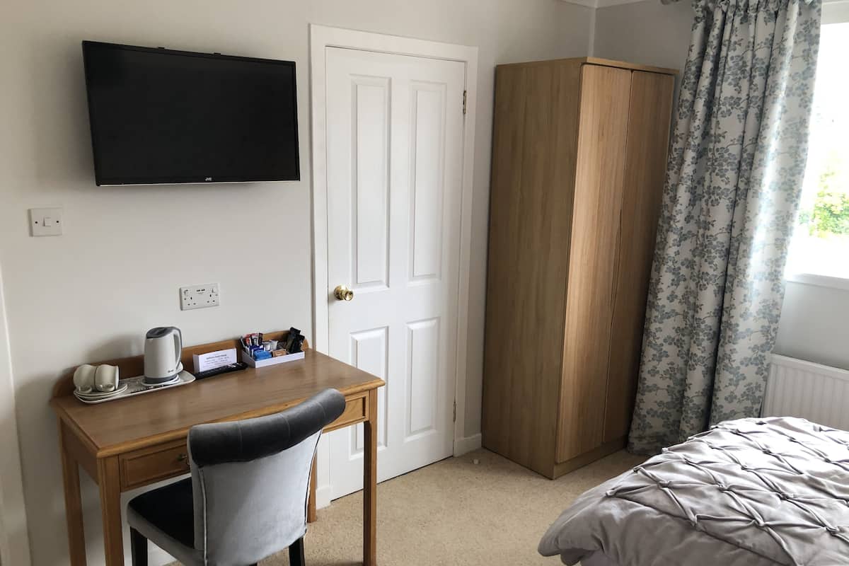 A bedroom with a bed, a desk with a chair, a wardrobe, and a TV mounted on the wall.
