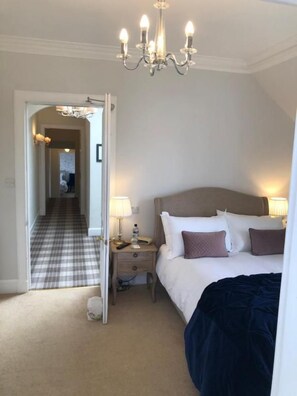 A hotel room with a bed, bedside tables, a chandelier, a carpeted floor, and a view of a hallway. - Ballifeary Guest House (Inverness)