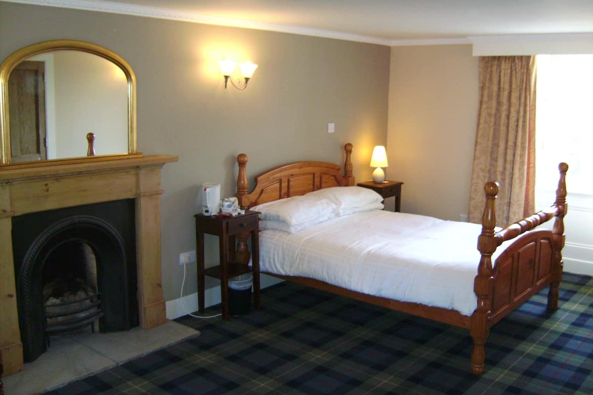 Une chambre à coucher bien aménagée, avec un lit en bois, une cheminée, une table de chevet et une lampe fixée au mur.