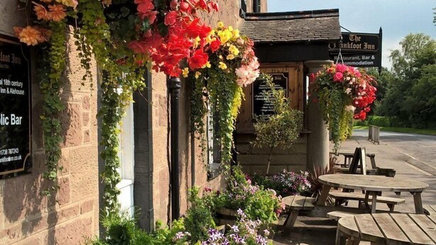 Un pub traditionnel, avec des jardinières suspendues et des tables à l’extérieur.
