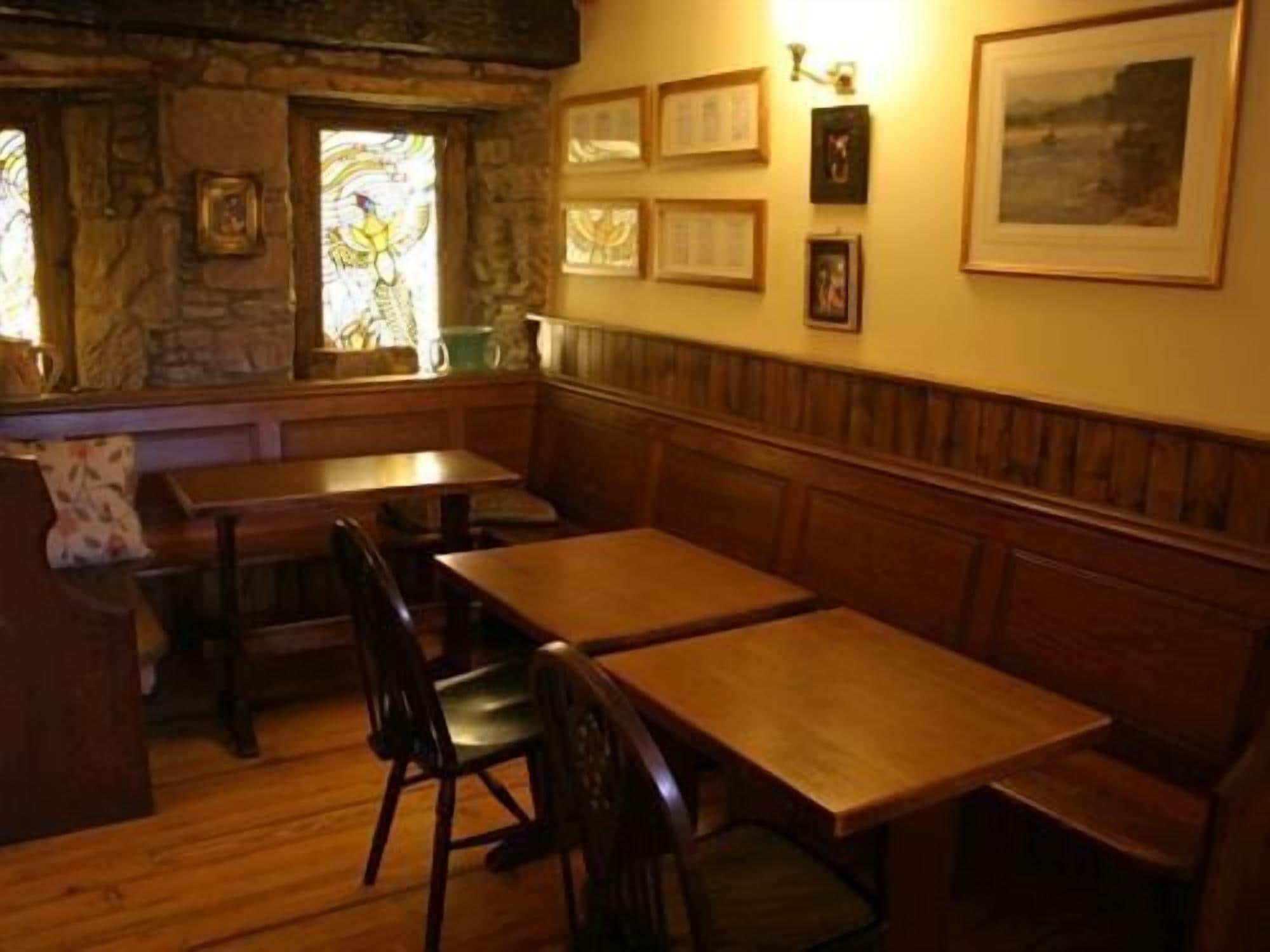 Un restaurant chaleureux avec des tables et des bancs en bois, des murs en pierre et des tableaux encadrés qui décorent les murs.