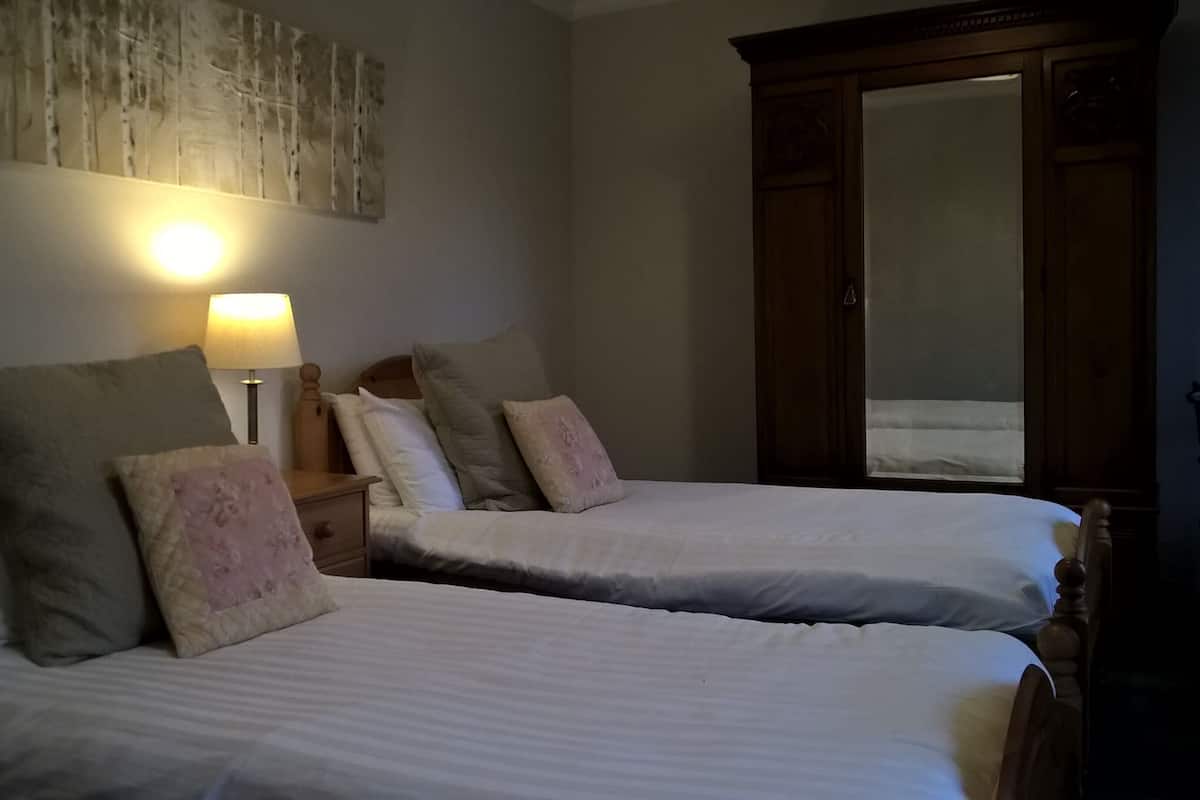 Une chambre avec deux lits, une table de chevet avec une lampe, une armoire en bois et un mur orné d’une œuvre d’art à texture particulière.