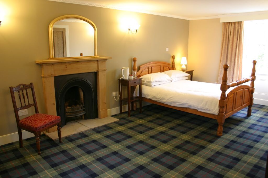 A bedroom with a plaid carpet, a wooden bed, a chair, a fireplace, and a mirror.