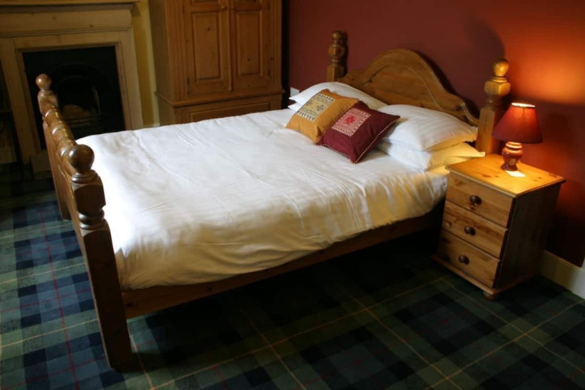 Un lit avec une tête de lit en bois, un sol à motifs écossais et une table de chevet avec une lampe.