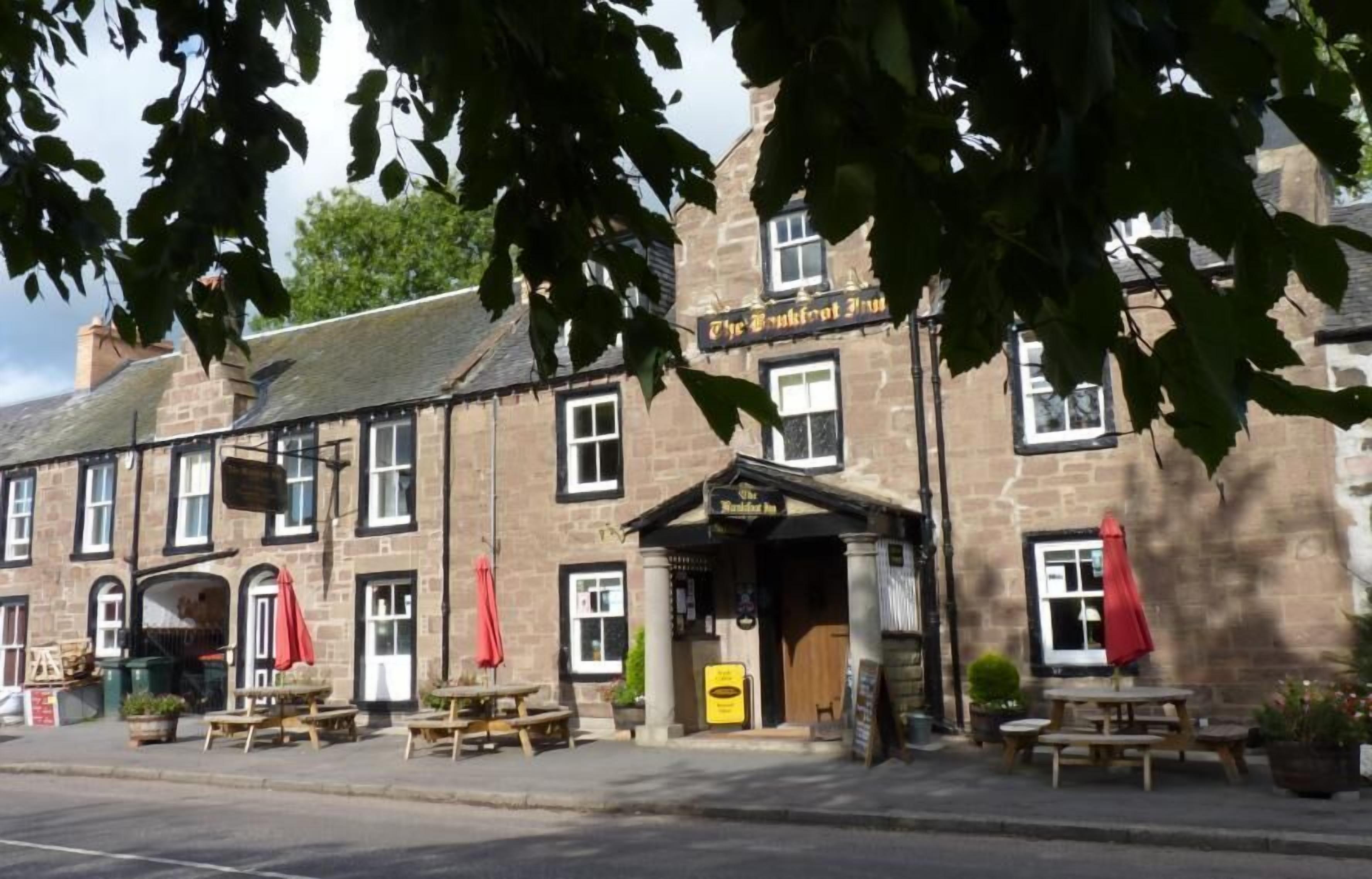 Un bâtiment traditionnel en pierre, avec une enseigne de pub, des tables à l’extérieur et un panneau indicateur.