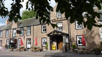 Un bâtiment traditionnel en pierre, avec une enseigne de pub, des tables à l’extérieur et un panneau indicateur.