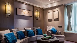 Una habitación de hotel moderna con sofá, sillones, una mesita de centro, obras de arte en la pared y una ventana con cortinas.