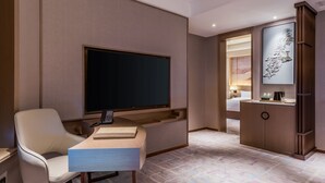 Habitación de hotel con televisor de pantalla plana, escritorio con teléfono, silla, mueble con espejo y cama con mesita de noche.