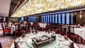 Un restaurante con mesas redondas, sillas rojas y un techo con lámparas colgantes.