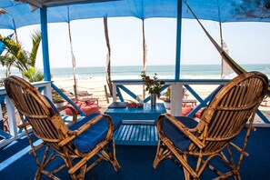 A beachside seating area with wicker chairs and a table, overlooking the ocean. - Cuba Agonda (Canacona)