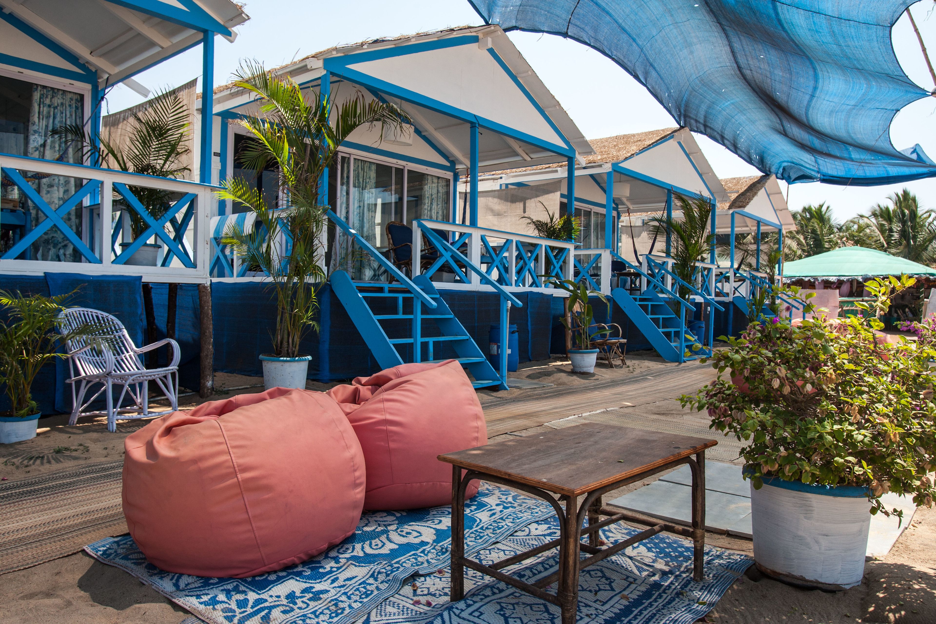 Un área de descanso frente a la playa, con una mesa de madera, dos pufs rosa y un tapete estampado.