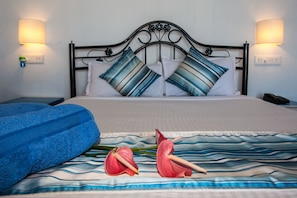 A neatly made bed with striped pillows, a blue blanket, and two red flowers on the bedspread. - Cuba Agonda (Canacona)
