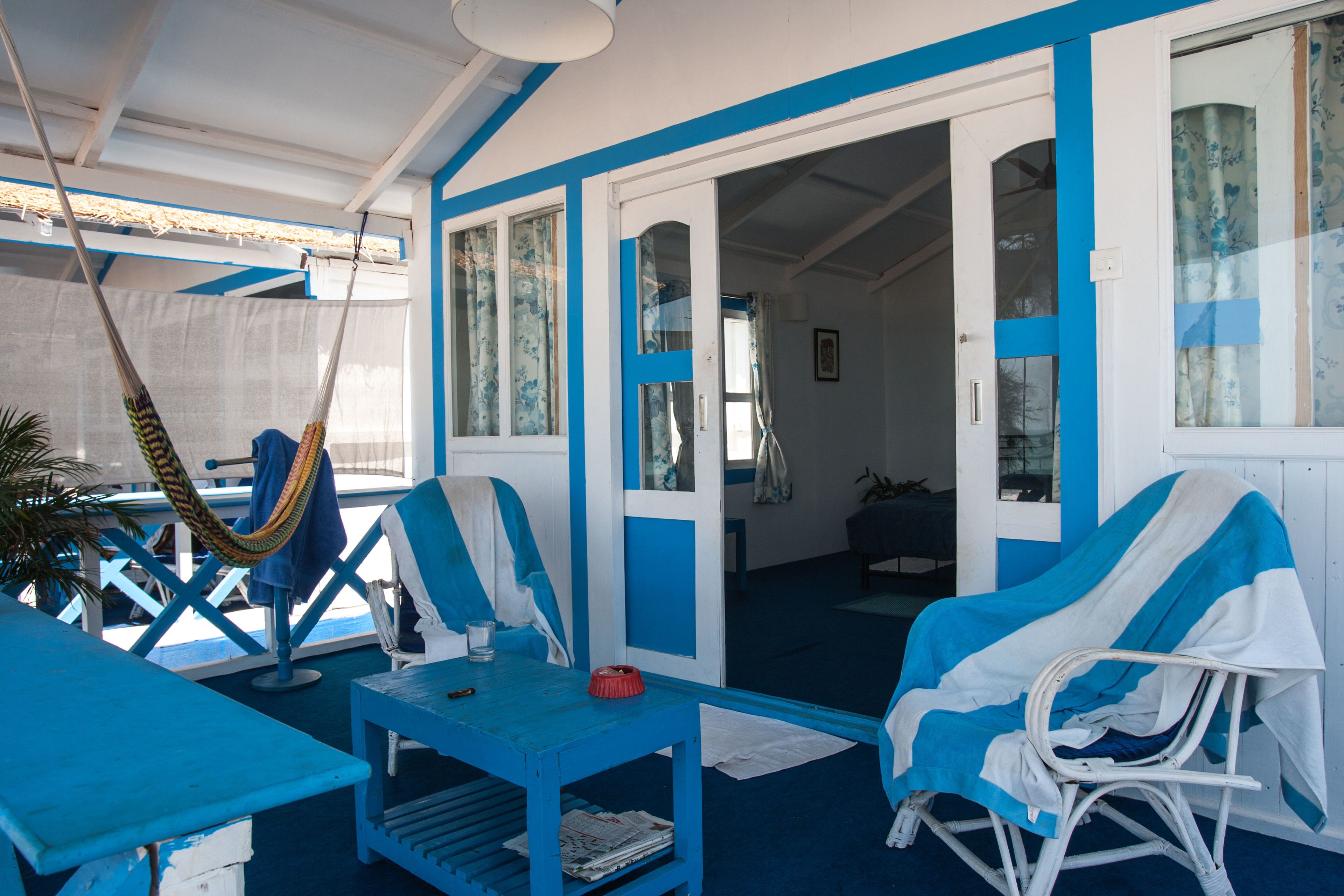 A room with a blue and white color scheme, featuring a hammock, a table with a newspaper, and two chairs.