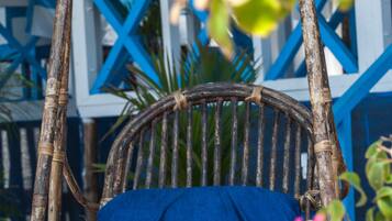A wicker chair with a blue cushion, tied with a rope, against a blue and white building with a geometric design.