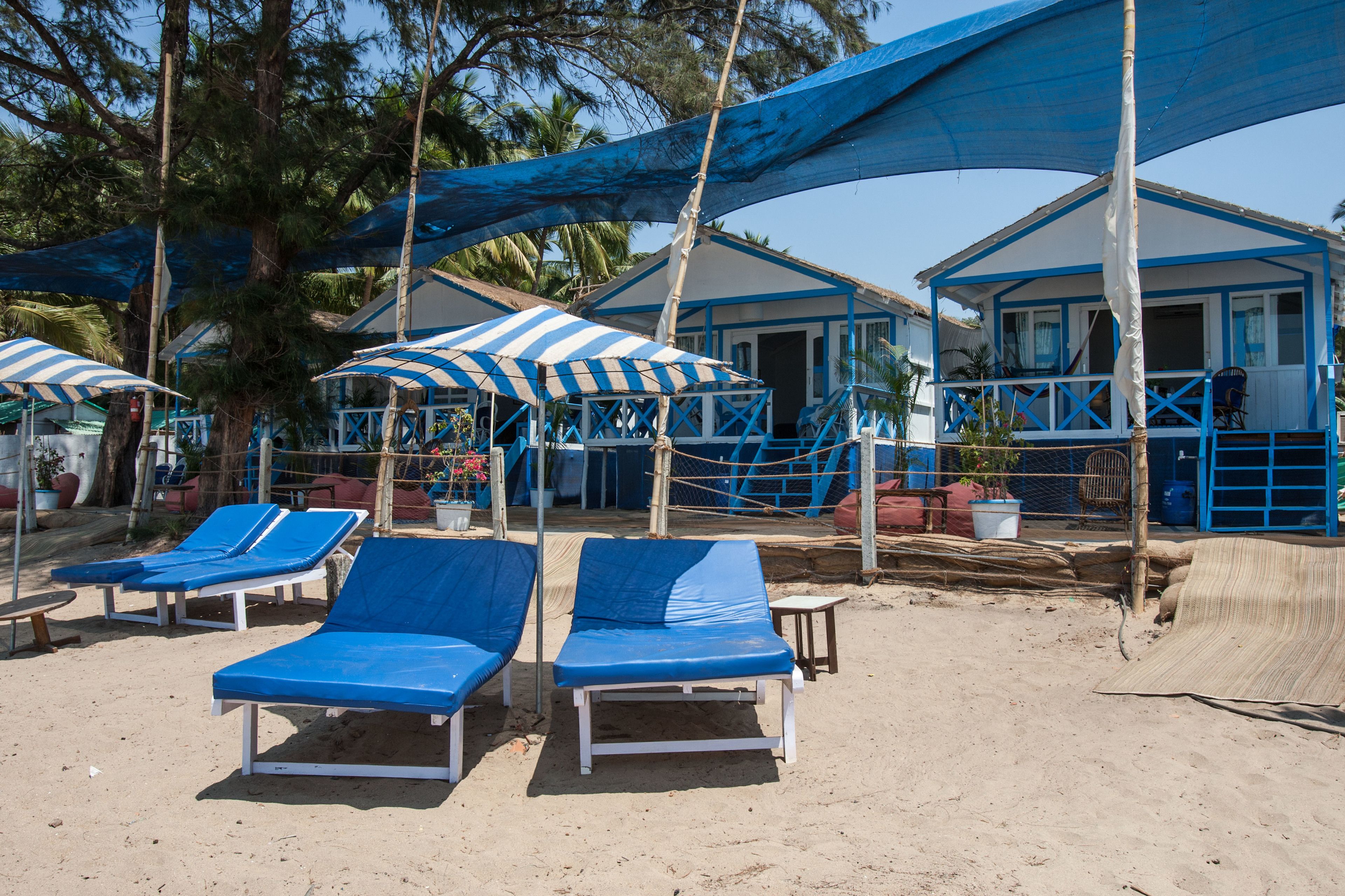Un complexe hôtelier en bord de mer, doté de parasols à rayures bleues et blanches, de chaises longues et d’un bâtiment aux couleurs bleu et blanc.