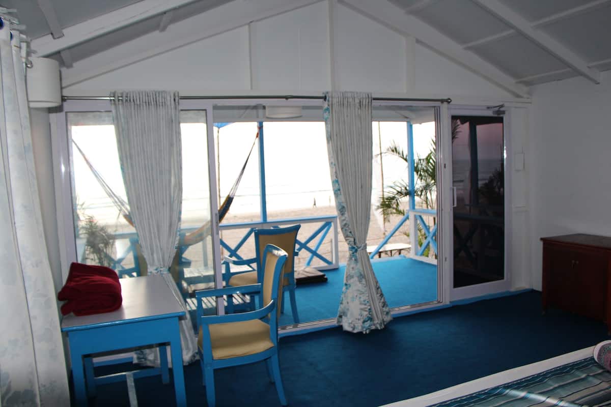 Una habitación con una mesa y sillas azules, una toalla roja y vistas a la playa a través de amplios ventanales.