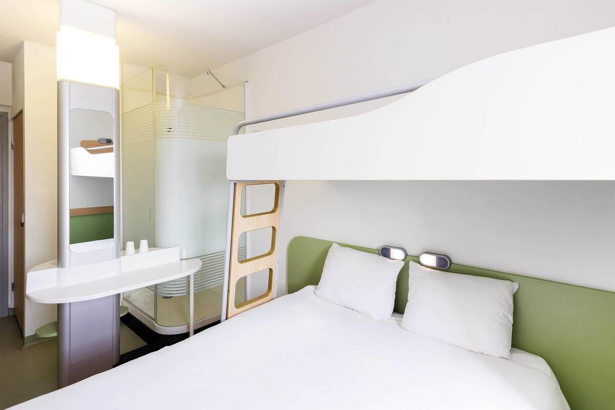 A bunk bed with a white headboard, a bedside table, and a mirror.