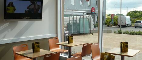 A restaurant with tables and chairs, a television on the wall, and a view of the street outside.