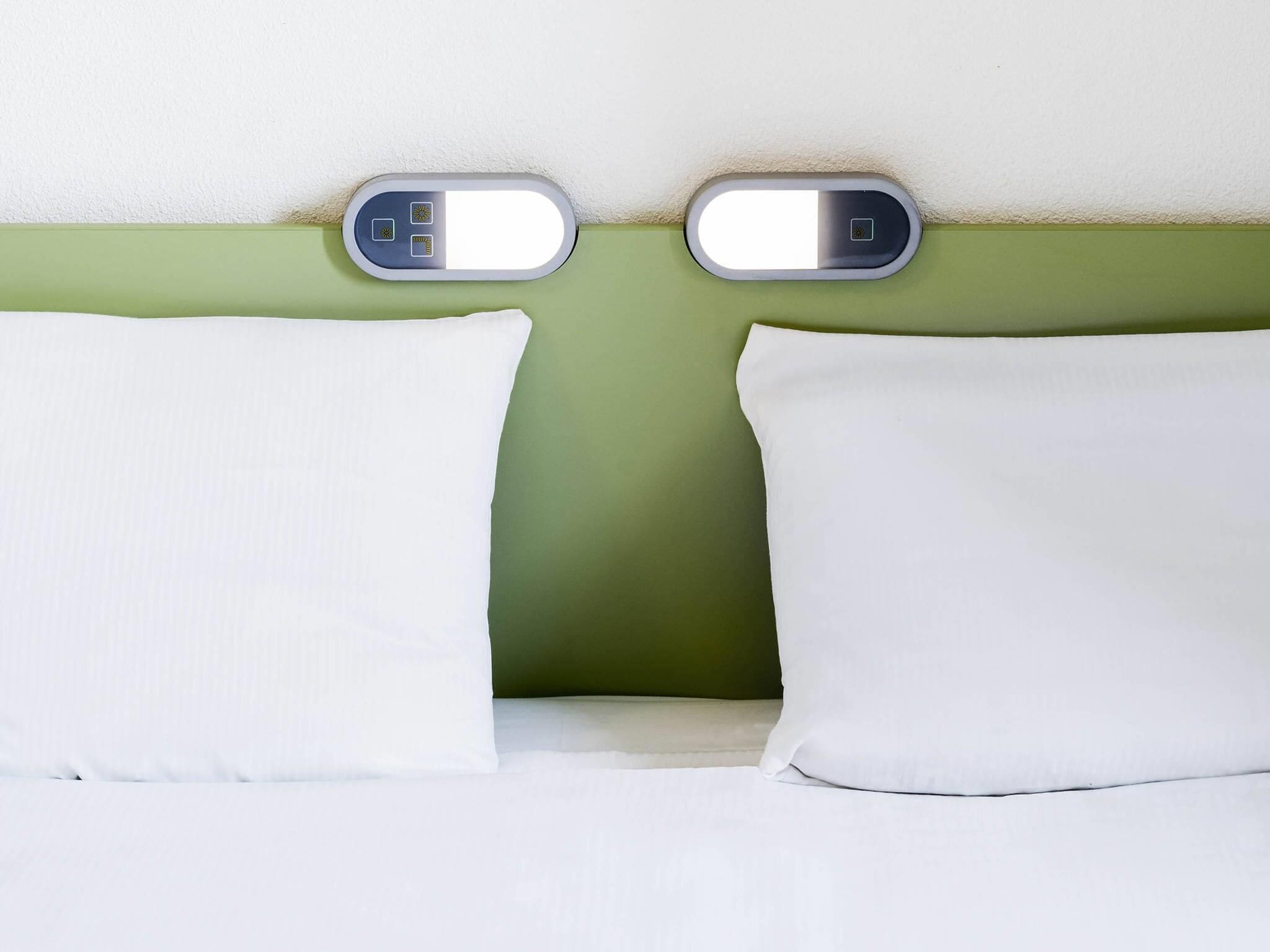 Una cama con almohadas blancas y una pared verde.