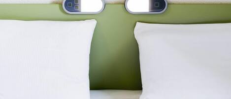 Una cama con almohadas blancas y una pared verde.