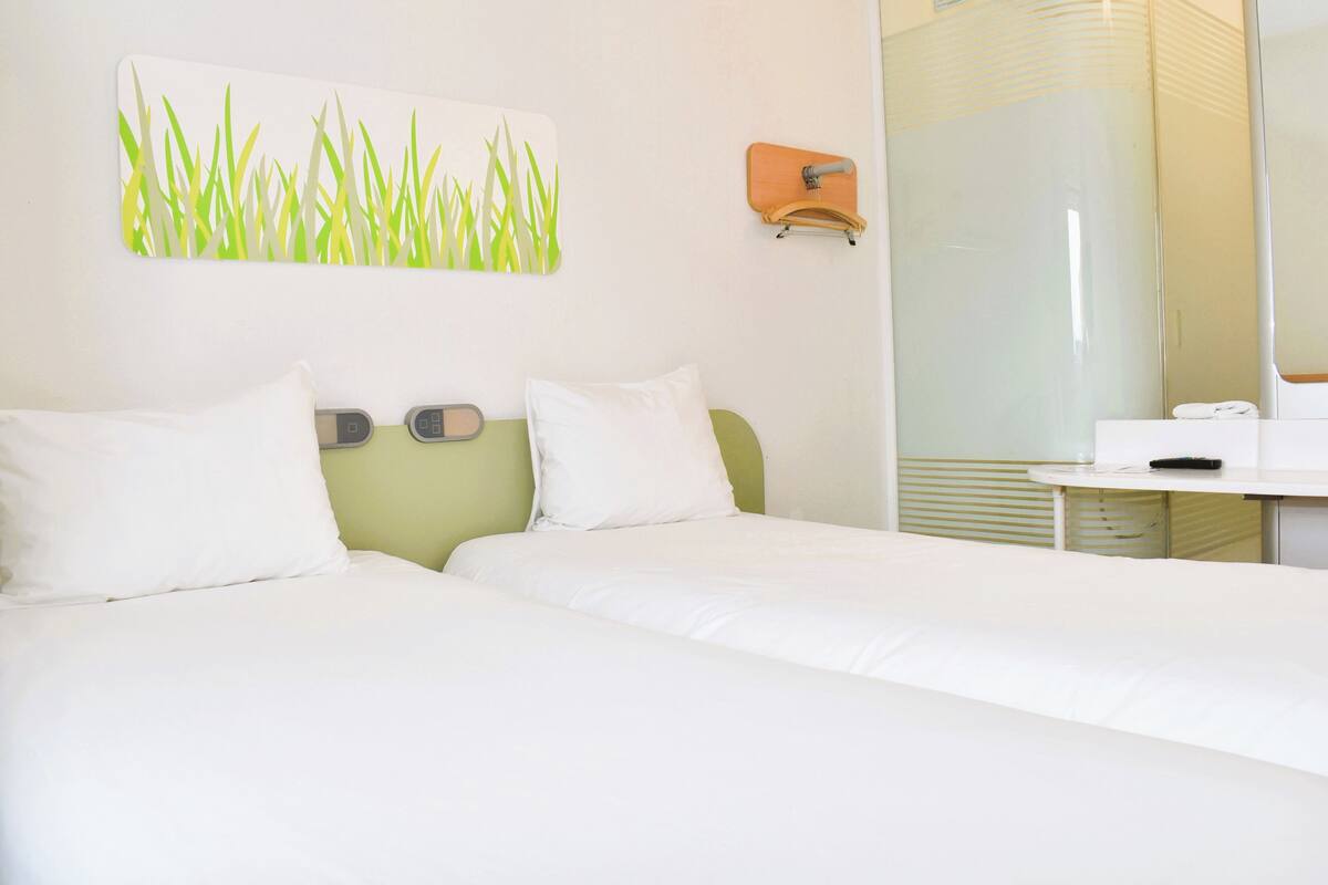 A hotel room with two beds, a bathroom with a glass shower, and a wall-mounted artwork.