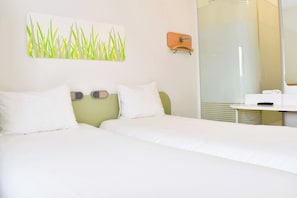 Ein Hotelzimmer mit zwei Betten, einem Badezimmer mit Glasdusche und einem an der Wand hängenden Kunstwerk.