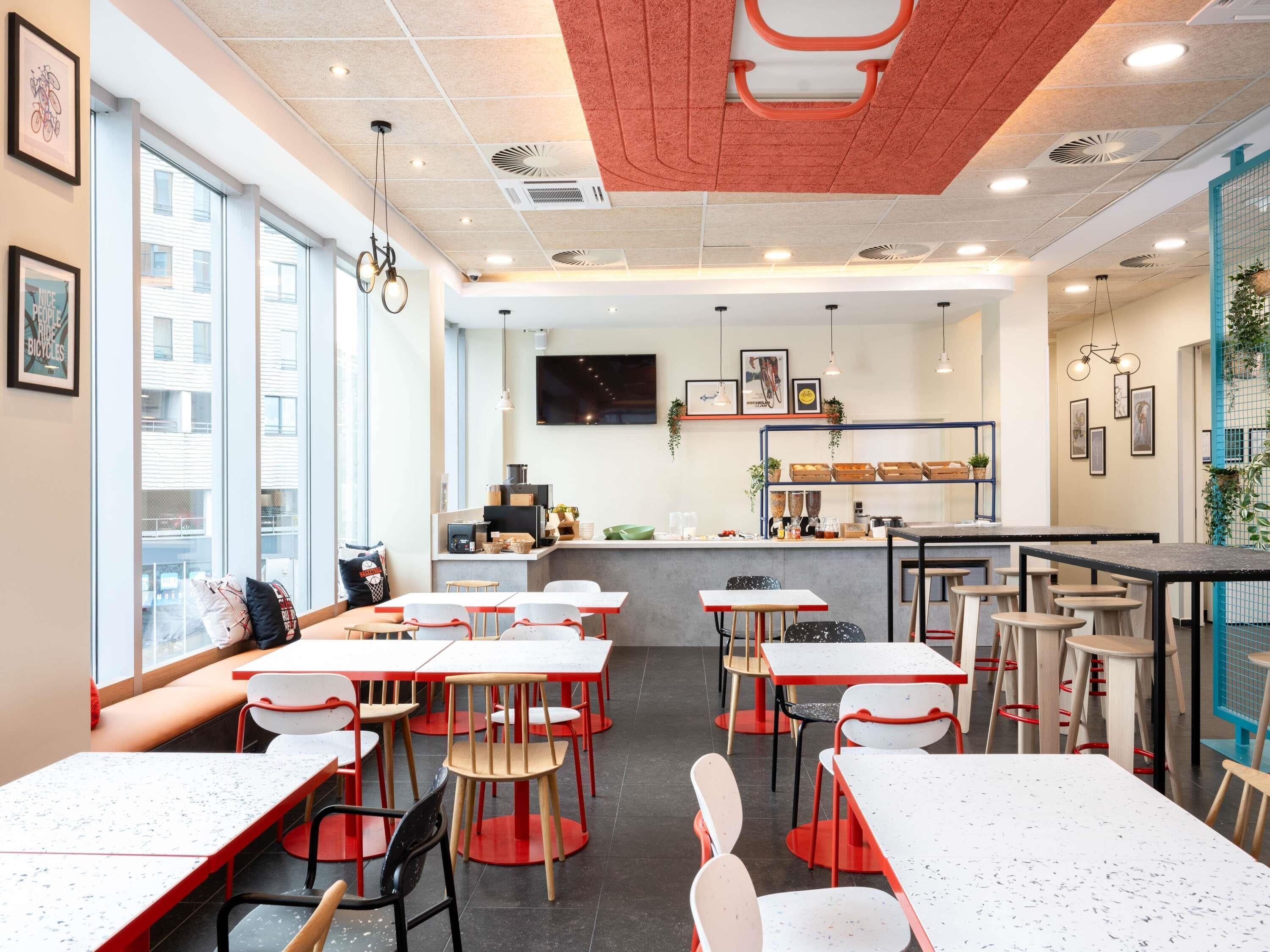 Un café moderno con varias mesas y sillas, una barra con una máquina de café y grandes ventanales que ofrecen vistas a la ciudad.