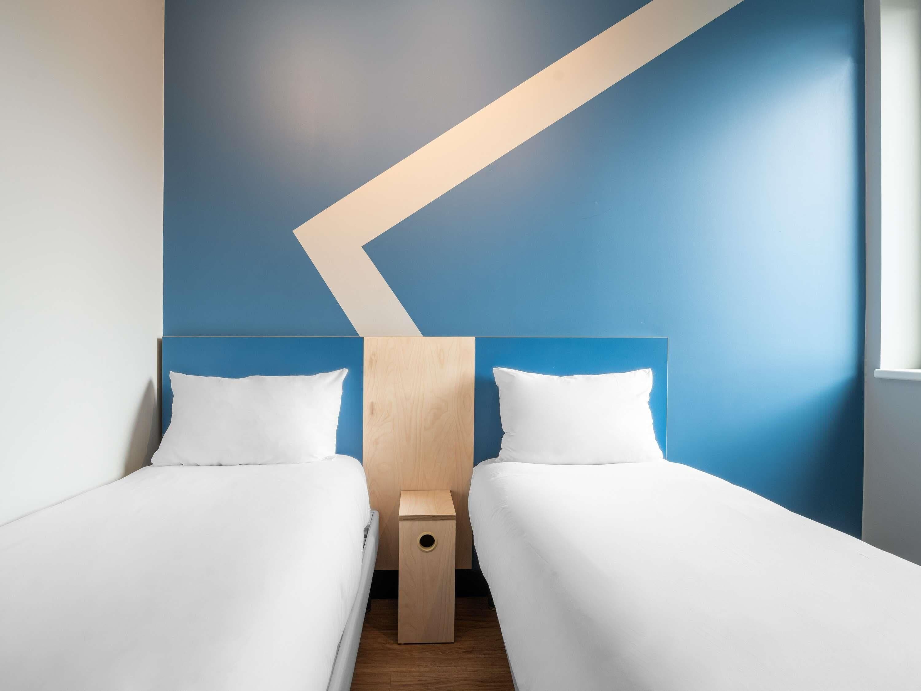 A room with two beds, a wooden nightstand, and a blue accent wall.