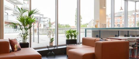 A modern hotel lobby with large windows, leather sofas, potted plants, and a view of the city.