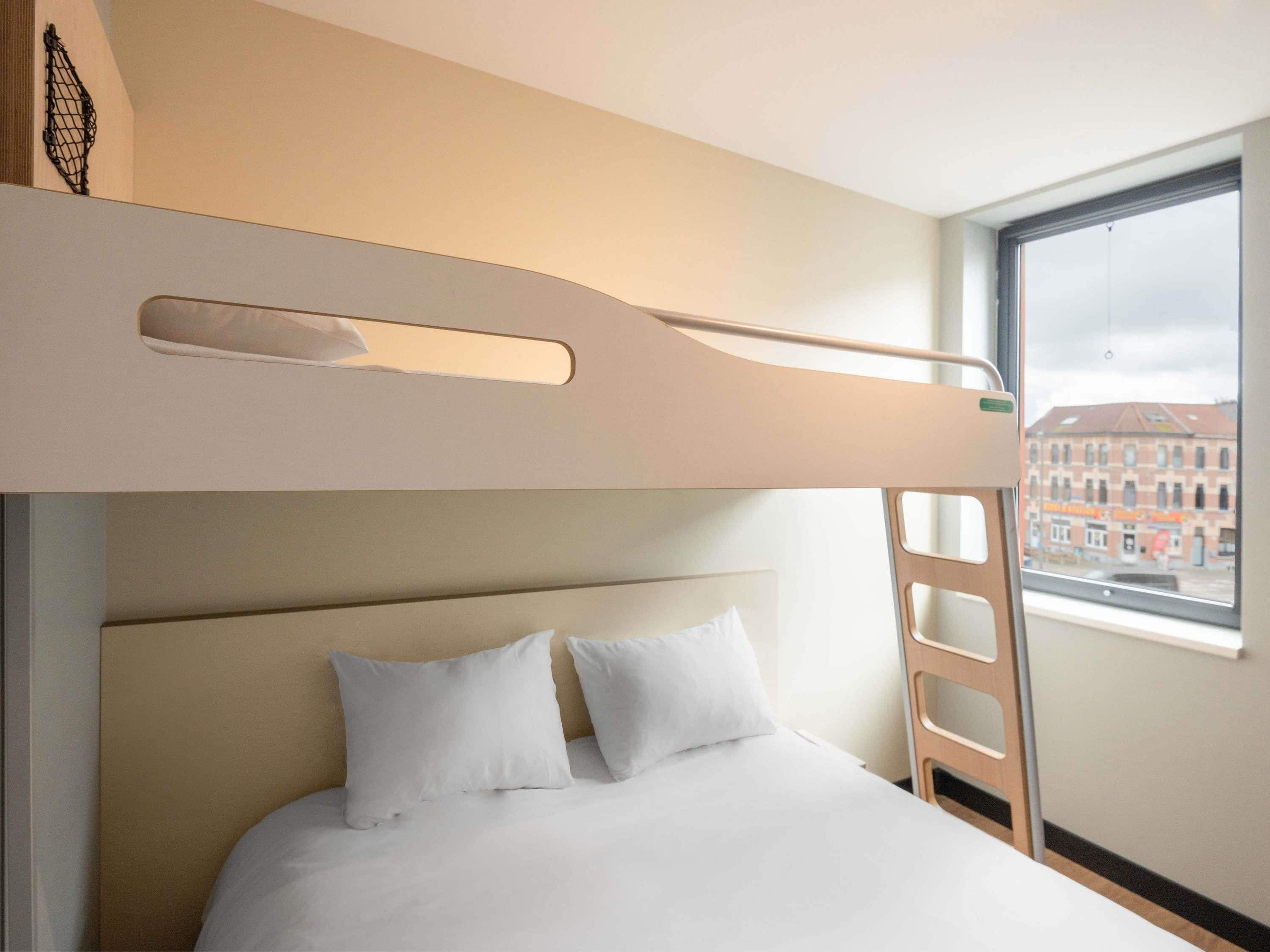 A bunk bed with a headboard, two pillows, and a window with a view of buildings.