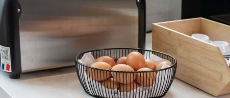 Una encimera de cocina con un tostador, un bol de huevos y una caja de madera con tazas.